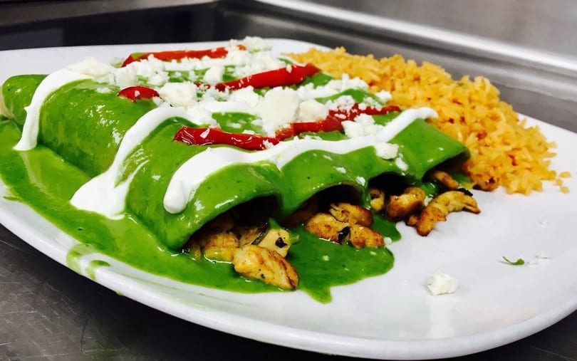Three green enchiladas topped with crema, cotija cheese, and red peppers, served with rice.