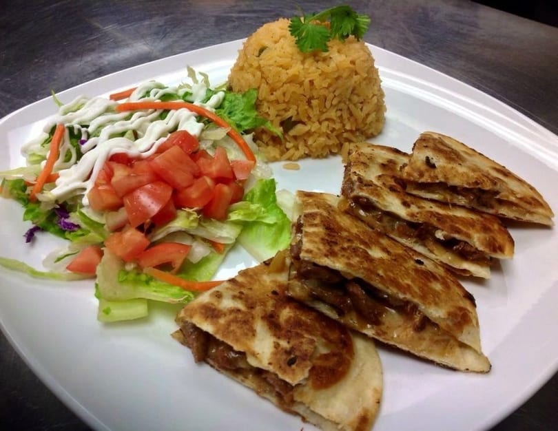 Quesadillas with rice and a side salad with tomatoes and dressing on a white plate.