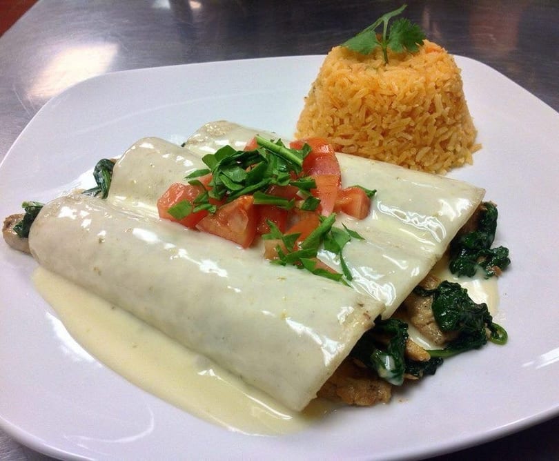 Three enchiladas covered in white sauce, topped with diced tomatoes and cilantro, served with rice.